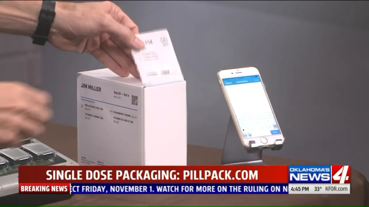 hand pulling a labeled single-dose medication packet from a white box beside a smartphone