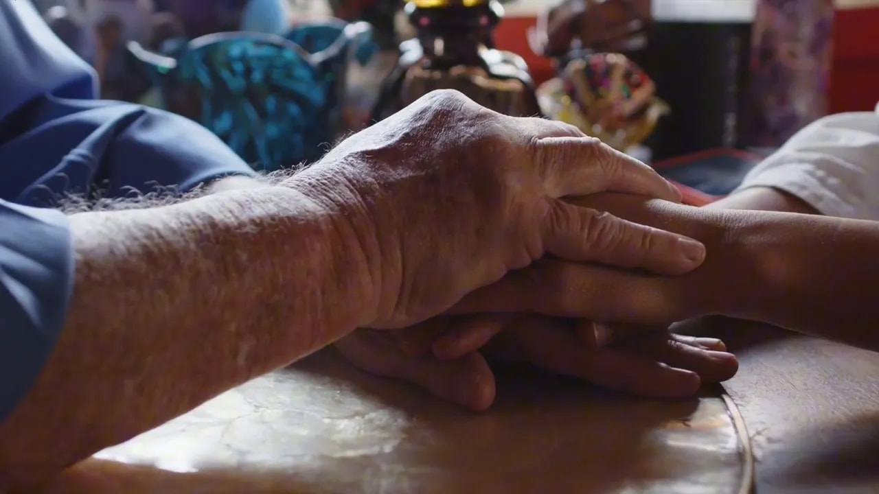An older hand resting gently on another person’s hand on a table
