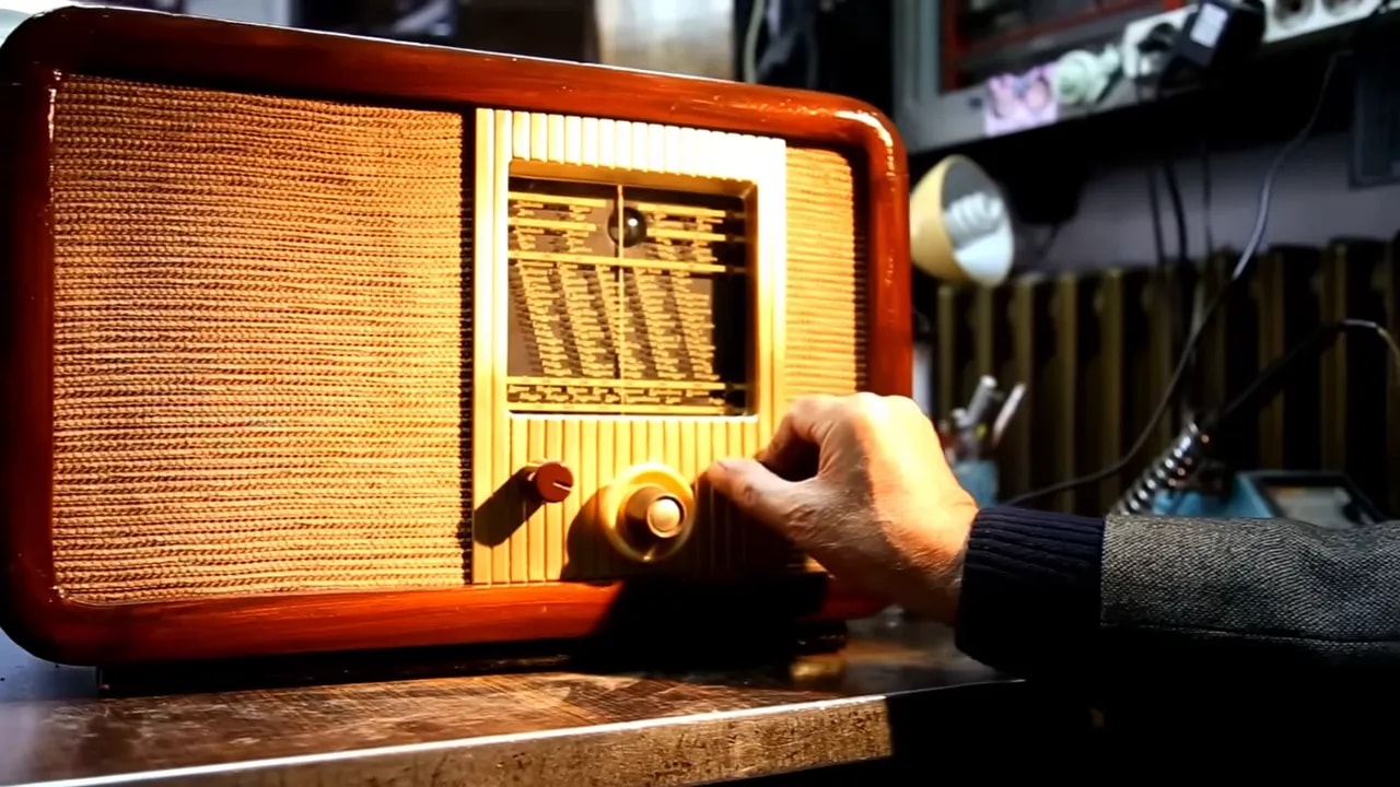 hand adjusting the tuning knob on a vintage wooden radio on a tabletop